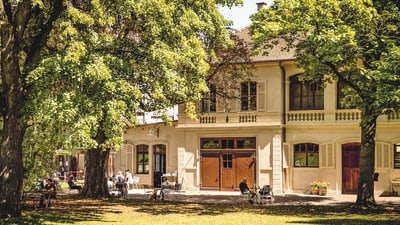 Historisches Gebäude mit Bäumen und Menschen im Garten.
