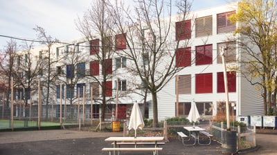 Moderner Schulgebäude mit Bäumen und Tisch im Vordergrund.