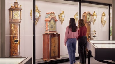 Zwei Personen betrachten Antikuhren in einem Museum.