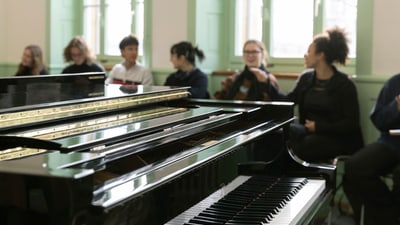 Schwarz glänzendes Klavier in einem Raum mit sitzenden Personen im Hintergrund.