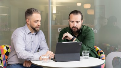 Zwei Männer sitzen an einem Tisch und arbeiten an einem Tablet.