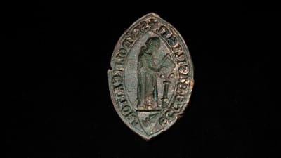 Mittelalterliches Siegel mit Figur und Inschrift auf schwarzem Hintergrund.