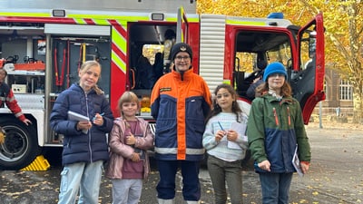 Gruppe von Kindern mit Feuerwehrfrau vor Feuerwehrauto im Herbst.