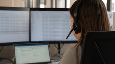 Person mit Headset, arbeitet am Computer mit mehreren Bildschirmen.