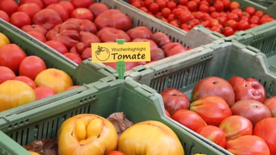 Kisten mit verschiedenen Tomaten im Markt mit Schild 'Wochenhighlight Tomate'.