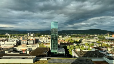 Stadtansicht mit hohem Glasgebäude und bewölktem Himmel.