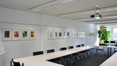 Konferenzraum mit Tischen, Stühlen und Wandbildern.