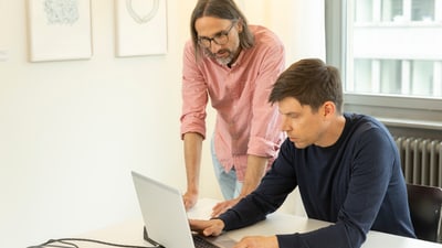 Zwei Männer arbeiten an einem Laptop in einem Büro.