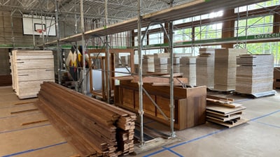 Holzstapel und Gerüst in einer Turnhalle mit Fenster und Basketballkorb.