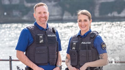 Zwei Polizisten in blauer Uniform mit Wasser im Hintergrund.