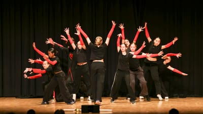 Gruppe Tänzer auf Bühne mit schwarzen Vorhängen.