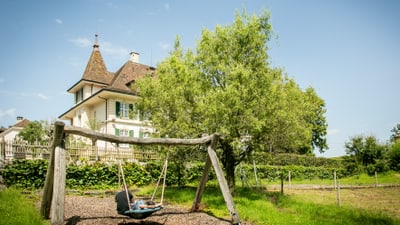 Haus mit Schaukelgestell im Vordergrund und Baum daneben.