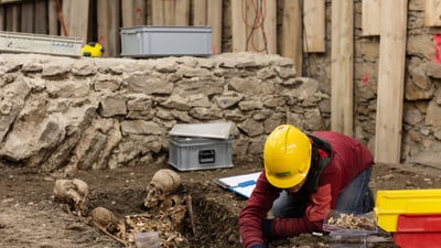 Arbeiter gräbt bei archäologischer Ausgrabung neben Skeletten.