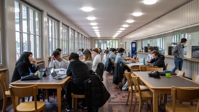 Menschen arbeiten in einer Bibliothek an Tischen mit Laptops.