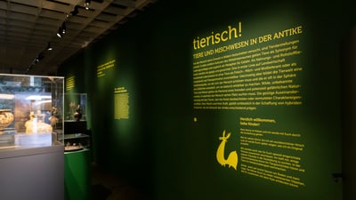 Ausstellungsraum mit grüner Wand und gelber Schrift über Tiere in der Antike.