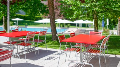 Rote Tische und Stühle im Freien bei einem Pool.