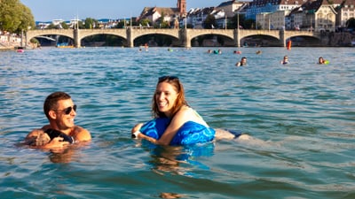 Menschen schwimmen im Fluss mit einer Brücke und Stadt im Hintergrund.