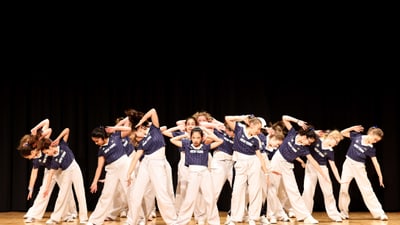 Gruppe von Tänzern in blauer Kleidung auf der Bühne in Formation.
