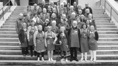 Gruppe von Freiwilligen von Tischlein deck dich in Schürzen auf Treppe vor Theater Café.