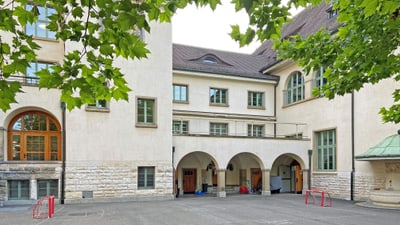 Schulhof mit Laubbaum und Gebäude mit Bögen.