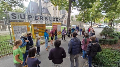 Gruppe von Menschen steht vor Infotafeln unter "SUPERBLOCK" Schild im Park.