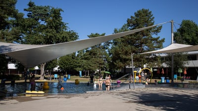 Kinder spielen im Freibad unter Sonnensegeln.