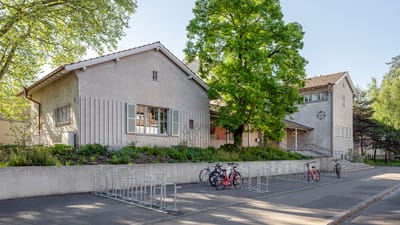 Gebäude mit Fahrradbügeln und grossen Bäumen.