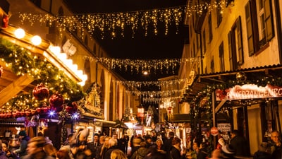 Weihnachtsmarkt bei Nacht mit Lichtern und Menschenmenge.",