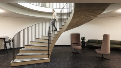 Person, die moderne Wendeltreppe hinaufgeht, mit Lounge-Bereich.",