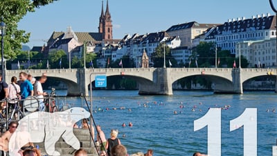 Menschen schwimmen im Fluss mit einer Brücke und Stadt im Hintergrund.