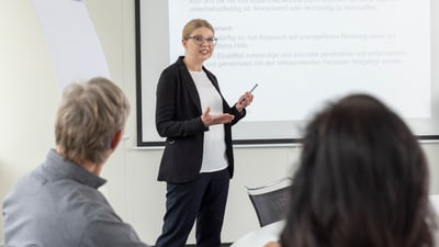 Person hält Präsentation vor Gruppe im Konferenzraum.