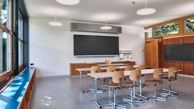 Klassenzimmer mit Pults, Stühlen und einem Fenster mit einem breiten blauen Fenstersims. 