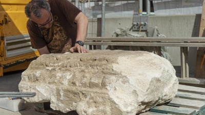 Mann untersucht grossen Steinblock auf Holzpalette.