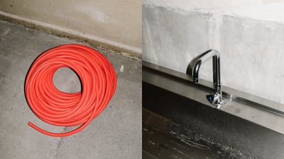 Rote Schlauchrolle auf Betonboden neben einem Wasserhahn an einer Wand.