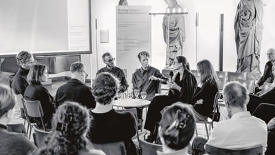 Diskussion in einem Sitzkreis mit mehreren Personen in schwarz-weiss.