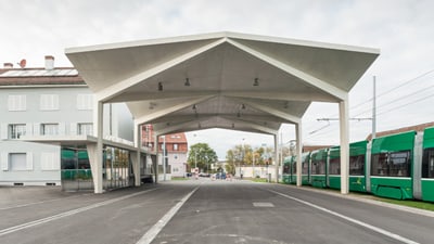 Gebäude und Tram dazwischen eine Strasse mit einer Überdachung aus Beton.