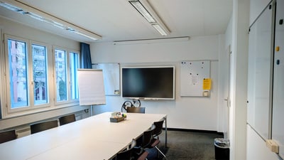 Konferenzraum mit Tisch, Stühlen und Smartboard.