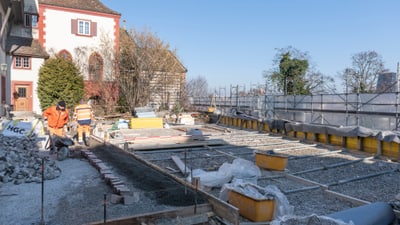 Zwei Bauarbeiter auf einer Baustelle vor einem alten Gebäude.