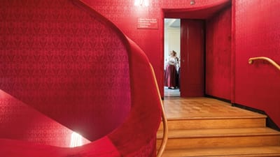 Treppe mit rotem Samt, Person im Türrahmen.