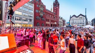 Eine riesige Menschenmenge auf dem Marktplatz, mit dem Rathaus im Hintergrund. Menschen tanzen vorne auf einer kleinen Bühne.