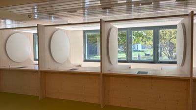 Moderner Raum mit grosser Holzschreibtischplatte, Akustikpanels und Fenstern.