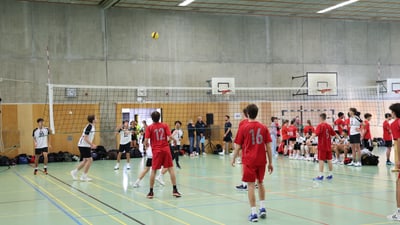 Volleyballspiel in einer Turnhalle mit zwei Teams und Zuschauern.