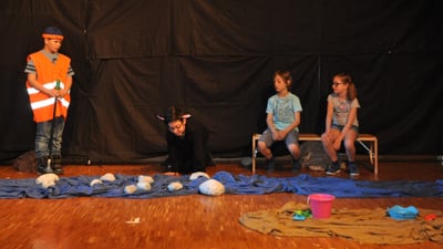 Kinder auf der Bühne in Kostümen bei einer Theateraufführung.",