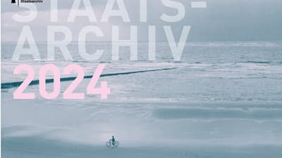 Person auf Fahrrad am Strand mit Ozean im Hintergrund, Staatsarchiv 2024 Schriftzug.