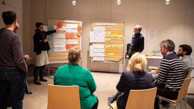Menschen in einem Meetingraum mit Flipcharts diskutieren.",