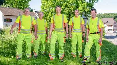 Fünf Männer in Warnkleidung im Freien.