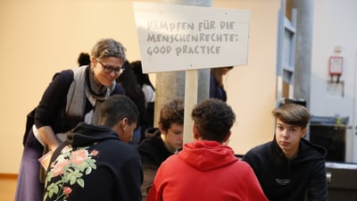 Jugendliche diskutieren unter dem Schild 'Kämpfen für die Menschenrechte'