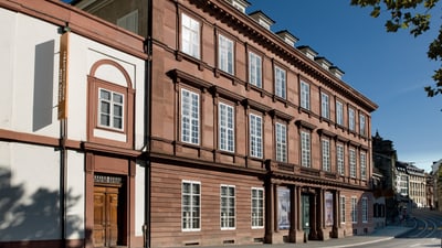 Historisches rotes Gebäude mit grossen Fenstern an einer Strassenecke.