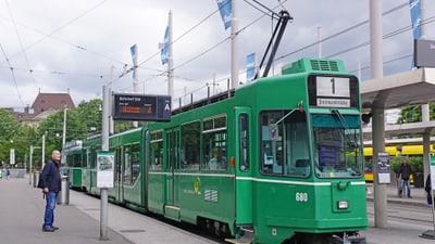 Grüne Strassenbahn an der Haltestelle mit wartendem Passagier und Anzeigetafel.