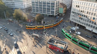 Foto des Aeschenplatzes mit Trams, Autos, zu Fuss gehenden Personen und Velos.